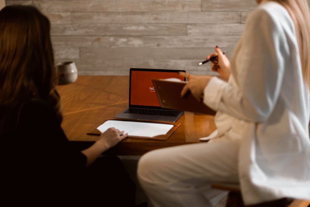 Reunião de consultoria da NÔH | BI: duas profissionais em uma mesa de trabalho, diante de um laptop com a marca NÔH | BI na tela