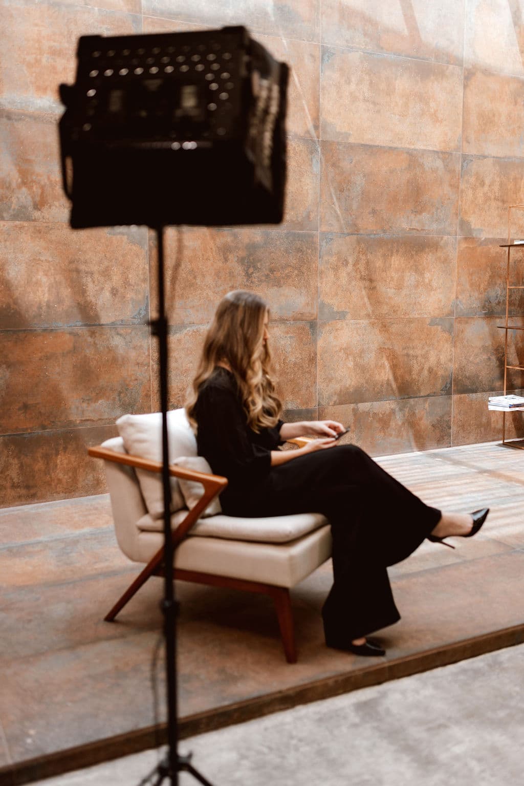 Lais Nohemann, fundadora da NÔH | BI, sentada em uma poltrona em um estúdio com parede terracota